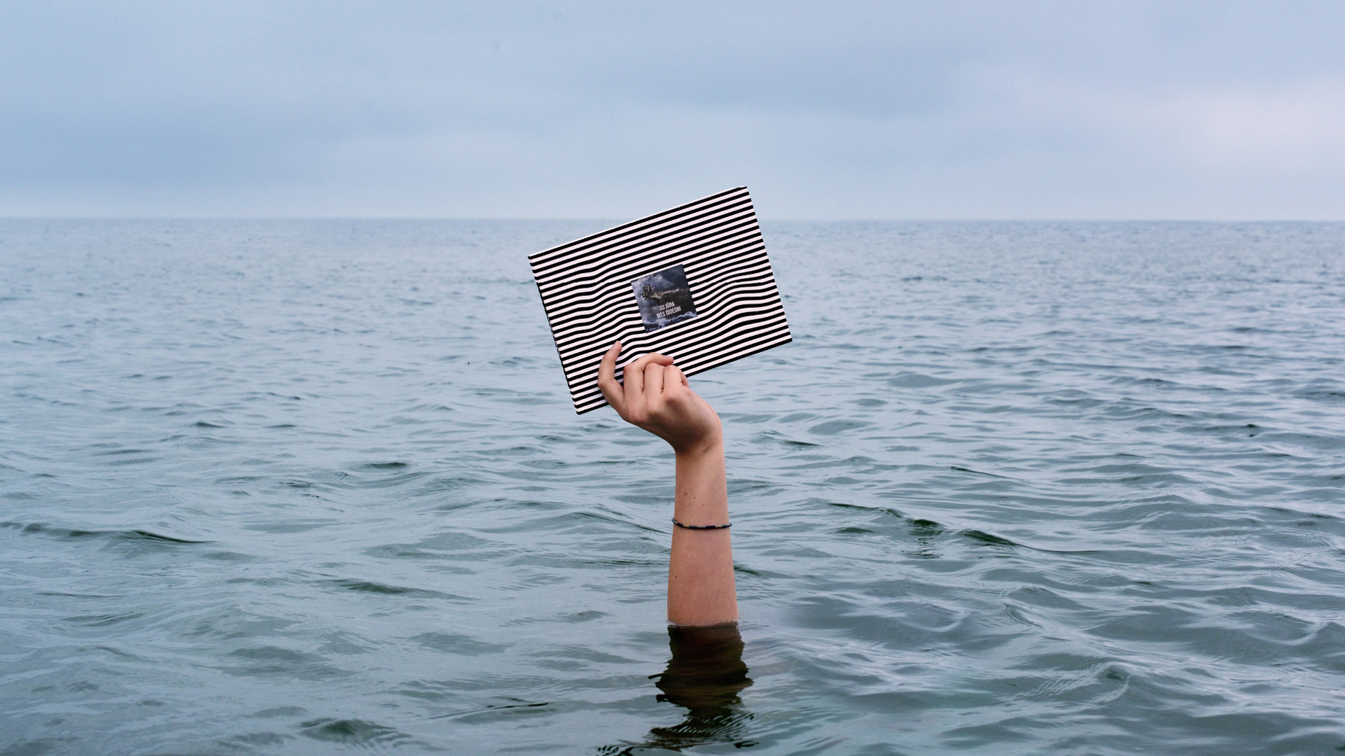 “Su jūra mes didesni” educational book held above the sea
